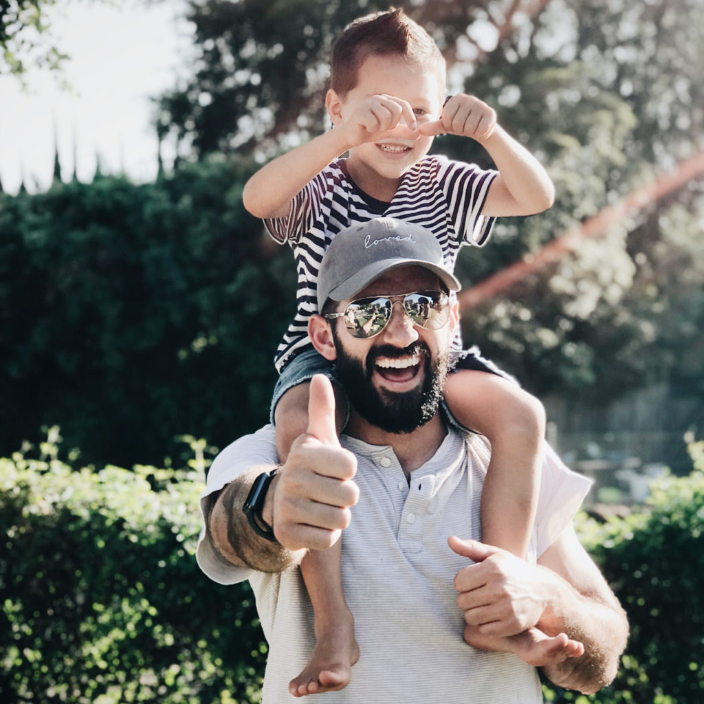 a man with his son on top of his shoulders giving a thumbs up